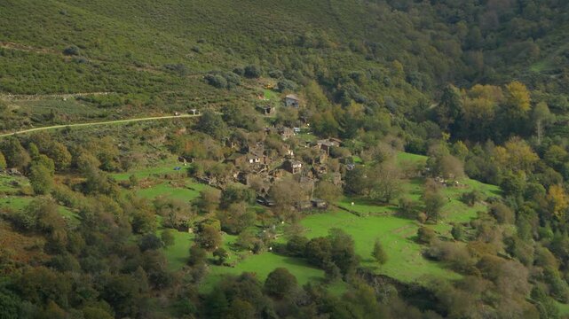 View across the green remains of Santoalla do Monte in Galicia, Spain, showing old stone houses and vegetation within the remote settlement affected by rural depopulation