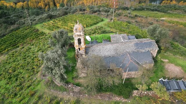 Drone view of the historic Santa Mar&iacute;a de Mones Church in Pet&iacute;n, Galicia, Spain, surrounded by rural roads, green fields and the mountainous landscape of Ourense