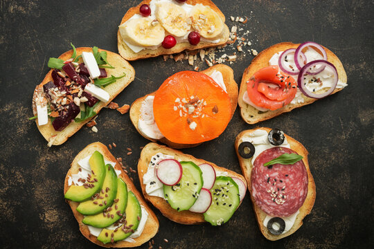 Set of different sandwiches on dark rustic background, with sausage, with salmon, with fruits and vegetables, top view, flat lay.