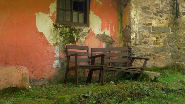 Rustic courtyard with old wooden chairs beside a weathered stone house in Santoalla do Monte, Galicia, Spain, preserving traces of traditional village life in the remote settlement.