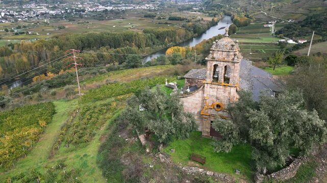 Drone view of the historic Santa Mar&iacute;a de Mones Church in Pet&iacute;n, Galicia, Spain, surrounded by rural roads, green fields and the mountainous countryside of Ourense.