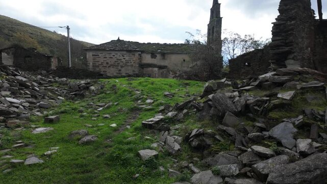 View across collapsed stone ruins toward the church tower of Santoalla do Monte in Galicia, Spain, documenting the decay and depopulation of the remote mountain village.