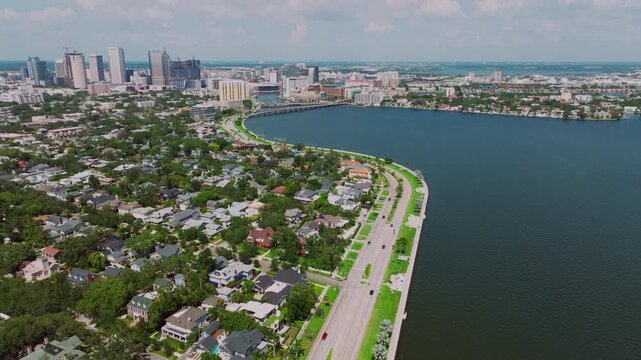 Aerial view of Bayshore Boulevard curving along Hillsborough Bay in Tampa's Hyde Park, with historic homes, lush greenery, and the downtown Tampa skyline in the distance.