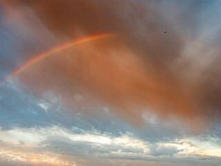 Obraz premium Faint Rainbow Beneath Dramatic Storm Clouds After Rain at Sunrise