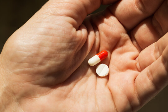Pills in human hand showing a red and white capsule and a white tablet. Healthcare and wellbeing.