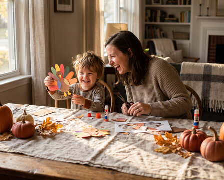 Playful mother and toddler crafting paper turkey at thanksgiving table