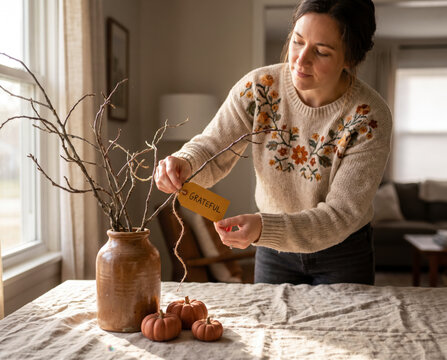 Reflective woman tying gratitude tag to autumn branches in ceramic vase