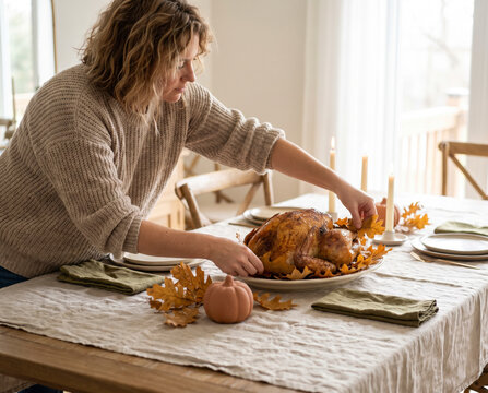Attentive woman placing autumn leaf beside roasted turkey on serving platter