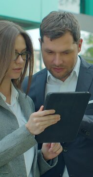 Vertical video. Business people standing near business center with digital tablet. Man and woman read news on Tablet Computer near office in morning.