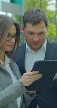 Vertical video. Business people standing near business center with digital tablet. Man and woman read news on Tablet Computer near office in morning.