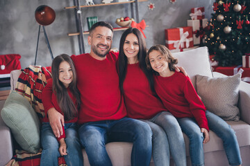 Naklejka premium Happy family in matching red sweaters celebrating Christmas together on a cozy sofa with decorated tree and presents in the living room