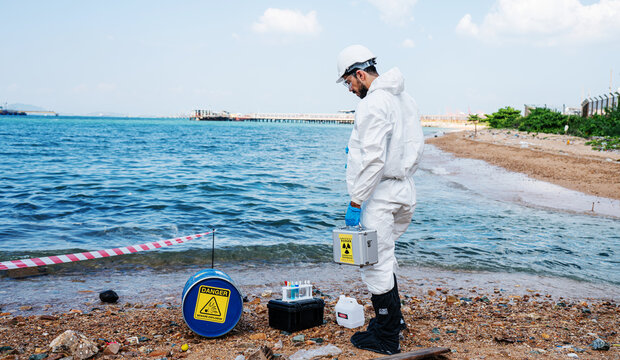 Scientists biologists and researchers in protective suits taking water samples from waste water from industrial. Experts analyze the water in a contaminated environment.