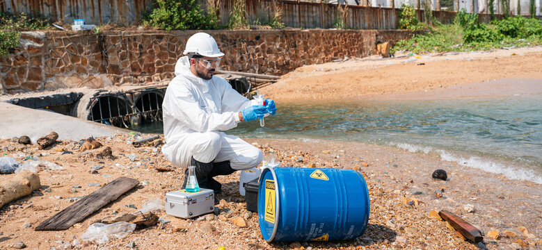 Scientists biologists and researchers in protective suits taking water samples from waste water from industrial. Experts analyze the water in a contaminated environment.