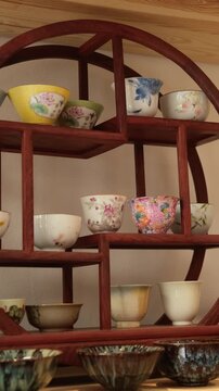 Ceramic teacups on wooden shelves arranged in rows with colorful patterns, a cozy display of artisanal kitchenware and traditional pottery collection.