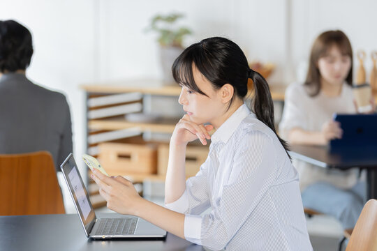 スマートフォンを見ながらノートパソコンで作業する日本人女性