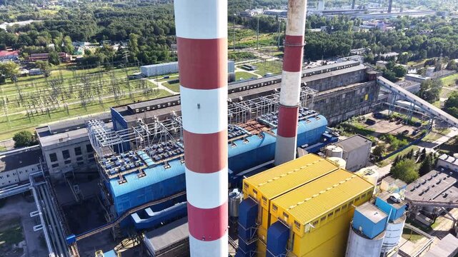 Aerial view of an industrial plant showcasing a series of large pipes and machinery, with blue roofs and structural elements visible, highlighting the complexity of the factory layout and design