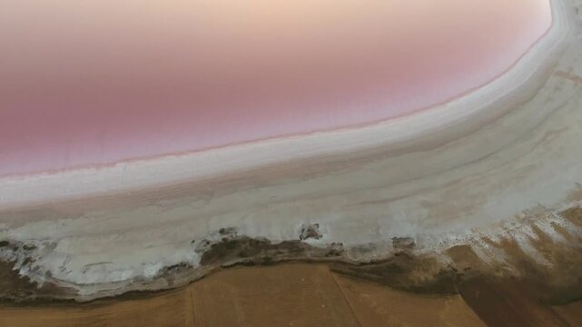 Aerial views trace a pink salt lake shoreline with shallow water, mineral textures, and color.