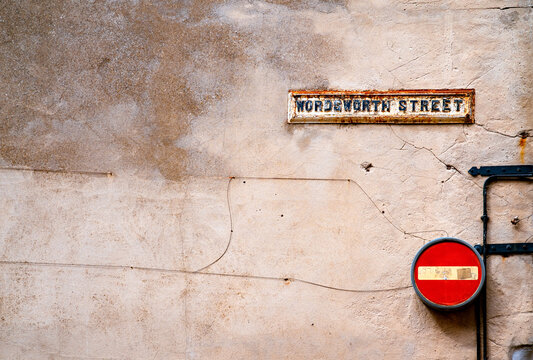 Weathered Wordsworth Street sign and red no entry traffic sign mounted on an aged, cracked facade in historic Lincoln, Lincolnshire, England.