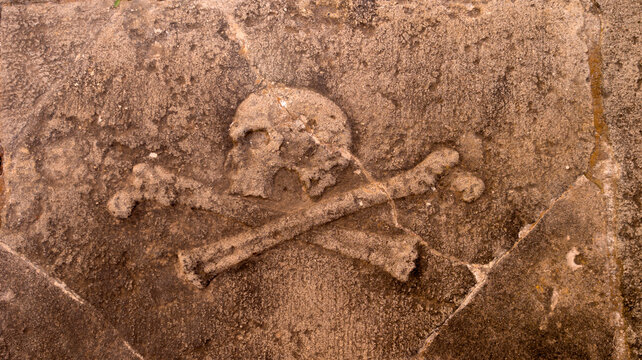 Losa de piedra con una calavera con tibias cruzadas tallada en relieve