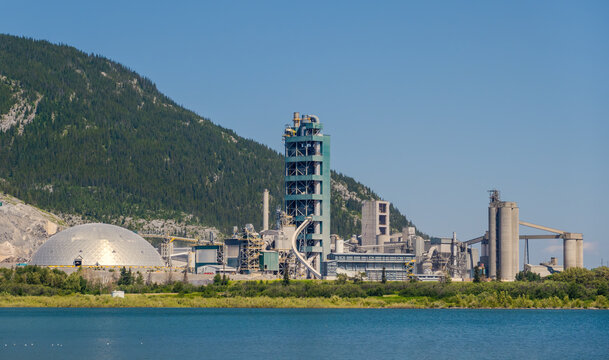 Exshaw, AB, Canada - Sept 14, 2026: Large industrial cement plant facility situated along a blue lake with mountain backdrop.