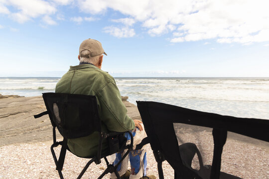 elderly man sitting in camp chair looking at ocean