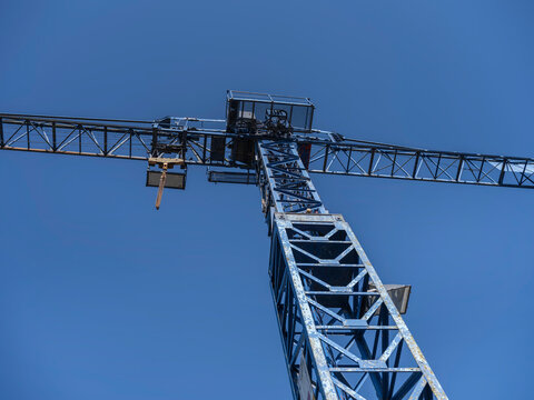 Looking straight up at the jib and trolley of a lattice tower crane, steel framework crossing a cloudless sky.