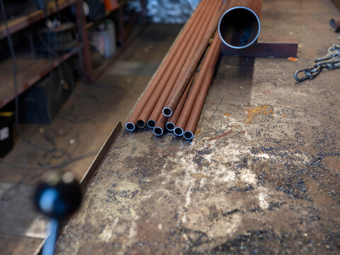 A bundle of copper pipes rests on a scarred steel workbench beside a square section tube, cut ready for installation.