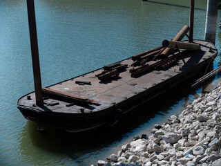 A flat steel barge moored at the quay carries lengths of pipe, materials waiting alongside a shipyard. © Victor