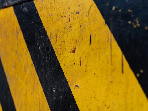 Scratched yellow and black diagonal stripes fill the frame, an abstract industrial pattern of caution markings.