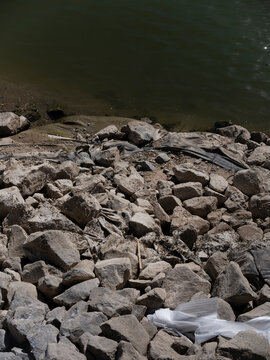 Loose riprap stones protect a sandy riverbank against erosion where the water meets the shore.