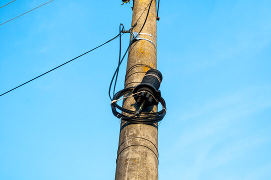 Coiled black cable wrapped around a wooden utility pole. Metal hardware and wires against a clear blue sky in a low angle view