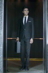 Confident Asian businessman in suit with briefcase standing in modern elevator © CungHao