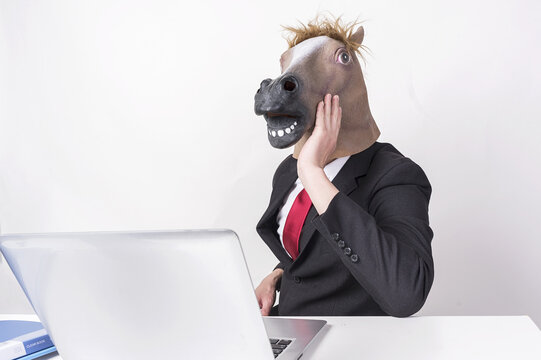 Businessman Wearing Horse Head Mask Working at Laptop in Office