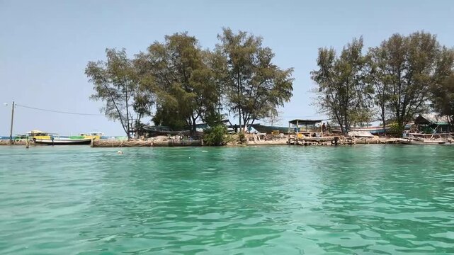 Small sandy island with pine trees viewed from clear sea water