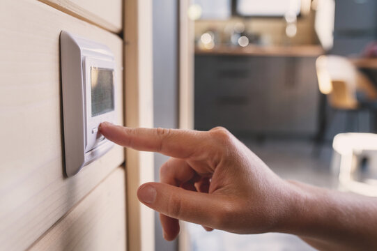 A woman's hand adjusts the temperature using a wall-mounted digital thermostat for underfloor heating. Climate control, energy-efficient home.