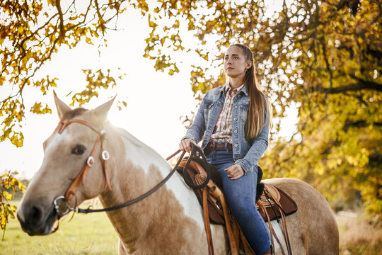 Woman riding horse in autumn nature. Cowgirl enjoying horseback riding and western lifestyle at countryside