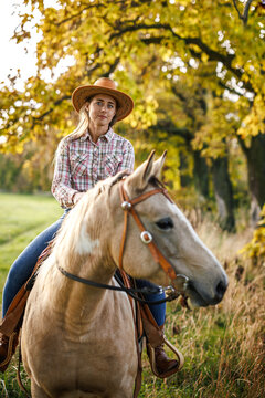 Woman in cowboy hat riding horse in autumn nature. Cowgirl enjoying horseback riding and western lifestyle at countryside