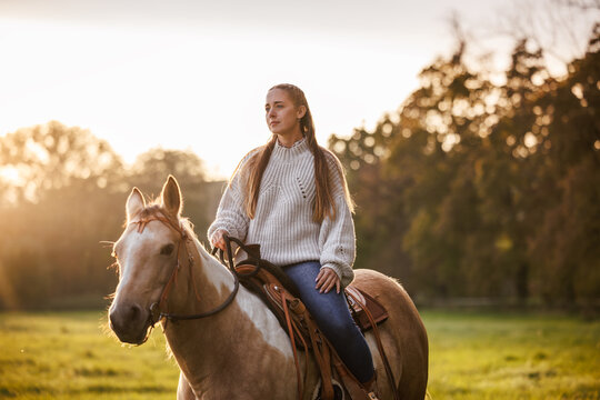Woman riding horse on pasture during sunset. Cowgirl enjoying horseback riding and western lifestyle at countryside