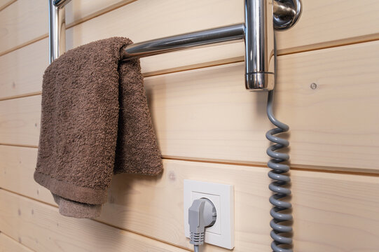 An electric towel warmer is plugged into a wall outlet in a hotel bathroom featuring wood paneling. Energy efficiency, smart resource use, energy-efficient home, climate control. closeup