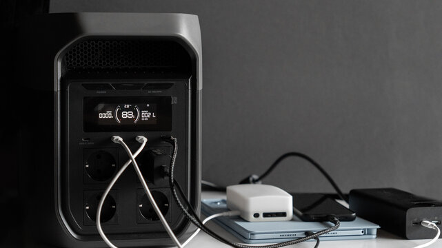 Portable power station with multiple cables for powering devices; charging smartphones, tablets, smartwatches, power banks, and flashlights. Concepts of backup power, energy independence