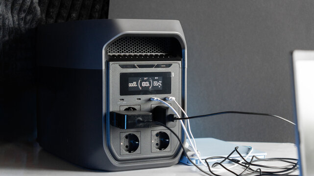 A computer and a tablet are charging from a portable power station, with power cables connected to the devices. A concept of backup power and energy independence. Electricity, energy storage