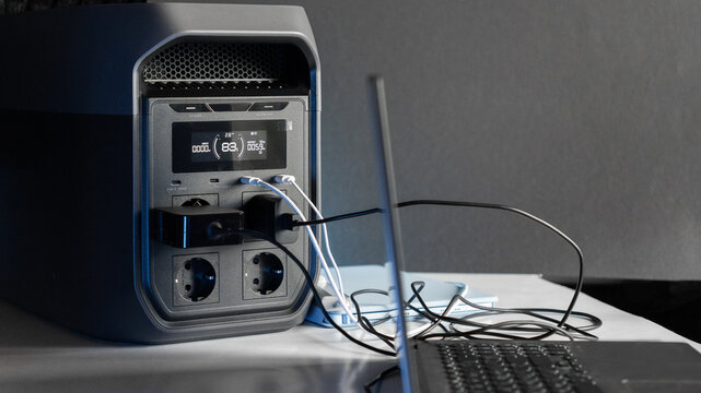 A computer and a tablet are charging from a portable power station, with power cables connected to the devices. A concept of backup power and energy independence. Electricity, energy storage