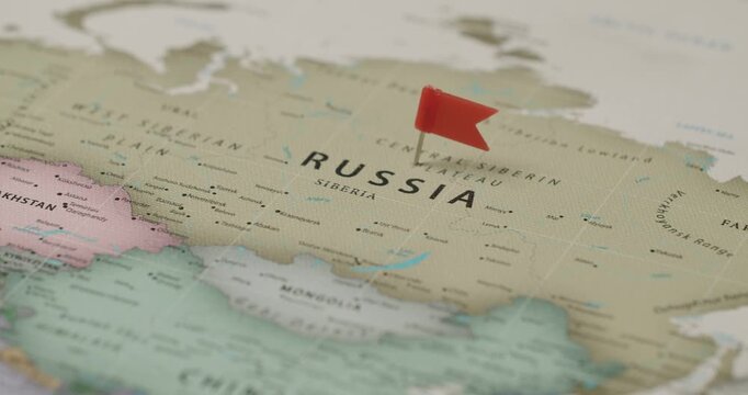 Person's hand marking Russia on a world map with a red flag pin, symbolizing travel planning, a destination, or a significant location in international politics and geography