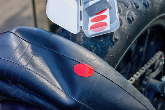 A person is applying a red patch to a bicycle tire using a repair kit on a sunny day in an outdoor setting