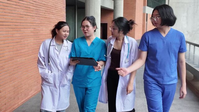 Medical students in scrubs walk together on a university campus while discussing information on a tablet, showing peer learning, teamwork, medical education, and young student lifestyle