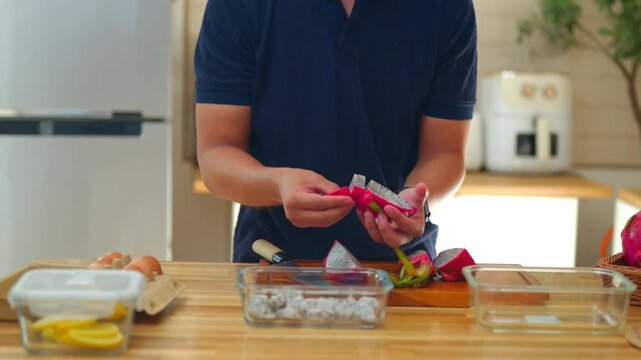 Man preparing dragon fruit meal prep in modern kitchen with glass containers on wooden counter