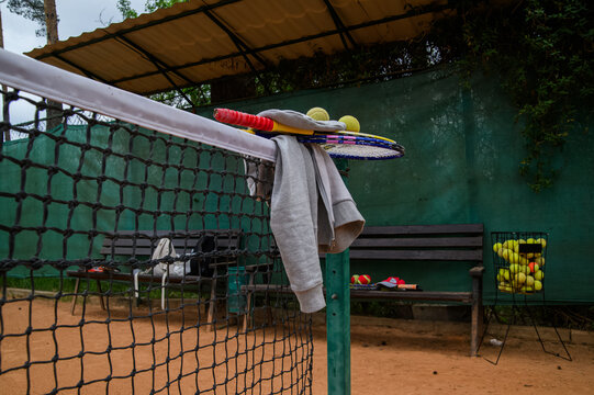 Tennis rackets, balls and sportswear resting on net at clay tennis court