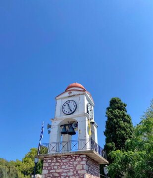 A low-angle view of the clock tower of the Agios Nikolaos church on Skiathos, set against a sunny blue sky.