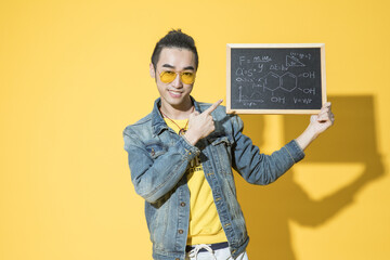 Fototapeta premium Happy young man holding a chalkboard with science formulas on yellow background