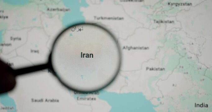 Hand holding magnifying glass focusing on the country of Iran on a digital map, highlighting its geographical location in the Middle East and its capital, Tehran, for study or analysis